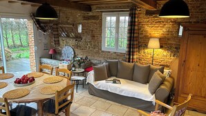 Une pièce rustique avec une table en bois, des chaises, un canapé et une fenêtre avec des rideaux.
