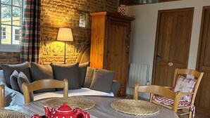 Une pièce chaleureuse avec un mur en pierre, des poutres apparentes, un canapé, une table à manger avec des sets de table et un service à thé rouge.