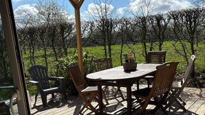 Une terrasse en bois avec une table ronde et des chaises, entourée d’une pergola.