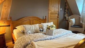 Une chambre à coucher avec un lit en bois, une literie à motifs, un panier en osier rempli de fleurs, une chaise et une armoire en bois.