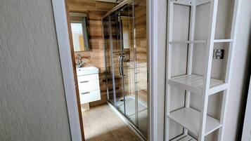 A modern bathroom with a glass shower enclosure, a white vanity, and a built-in shelving unit.