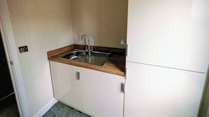 Une petite cuisine équipée avec un évier en acier inoxydable, un plan de travail en bois et des placards blancs.
