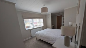 Une chambre à coucher comprenant un lit, une lampe de chevet, un radiateur, une fenêtre avec des stores et une porte donnant sur une autre pièce.