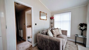 Un salon avec un canapé beige, un miroir, un radiateur et une fenêtre avec des stores.