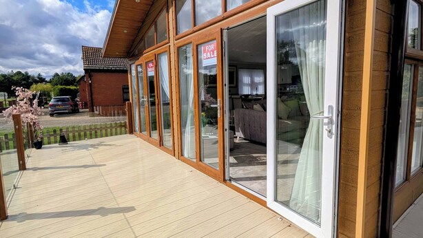 Un bâtiment moderne doté de grandes portes et fenêtres en verre, d’une terrasse en bois et d’une pancarte « À vendre ».