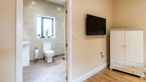 A bathroom with a toilet, sink, and window. There is a TV mounted on the wall and a white cabinet. - The Stables Cottage With Hot Tub - NO PE (Doncaster)