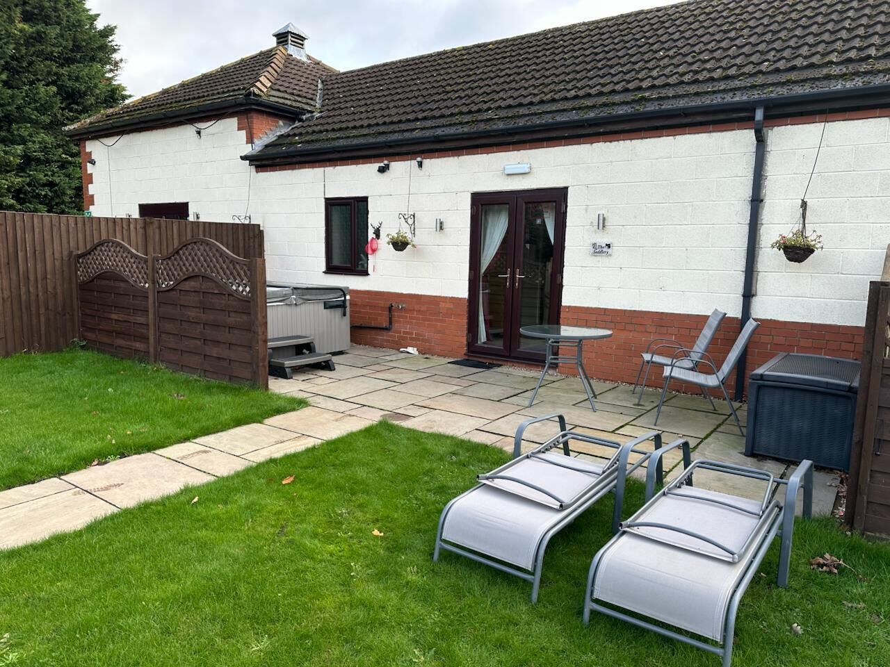 A house with a patio area featuring two reclining chairs, a small table, and a barbecue grill.