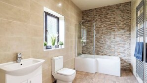 Un baño moderno con un lavabo, inodoro y bañera blancos, un box de ducha de vidrio y una pared con diseño de ladrillo.