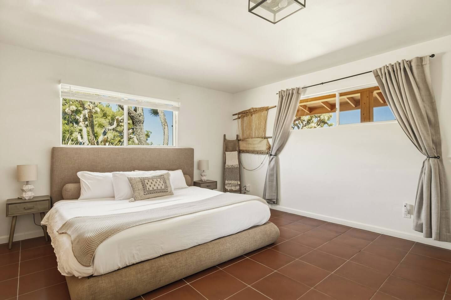 Une chambre avec un grand lit, une table de chevet, une fenêtre avec des rideaux et une vue sur les arbres.
