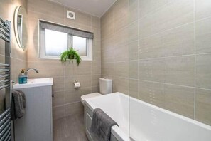 A modern bathroom with a bathtub, a sink, a toilet, and a window with a plant. - Beck Cottage Windermere (Windermere)