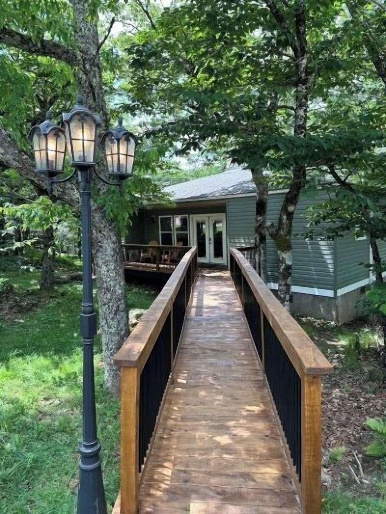 A wooden bridge leading to a house with a porch, surrounded by trees.