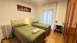 Une chambre avec deux lits, un bureau, une chaise, un radiateur et un tableau au mur.