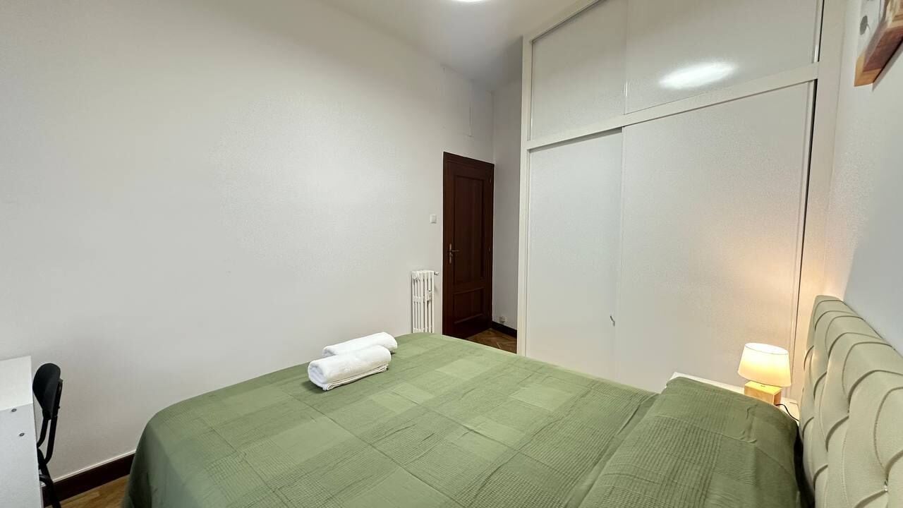 Un dormitorio con cama, un radiador, una puerta y una mesita de noche con lámpara.
