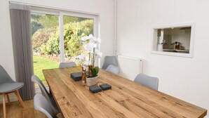 Un comedor moderno con una mesa de madera, sillas grises y vistas a zonas verdes al exterior.