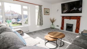 Una sala de estar con un conjunto de sofá, una chimenea, un televisor y vistas al exterior.