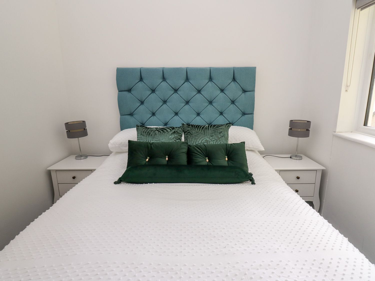 A neatly made bed with a tufted headboard, two bedside tables with lamps, and a window on the right.
