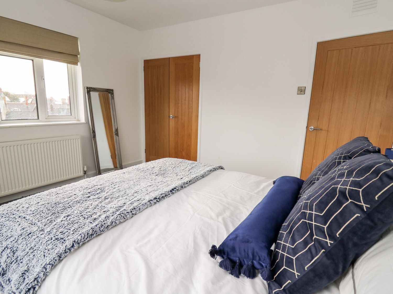 A bedroom with a bed, two doors, a window, and a radiator.