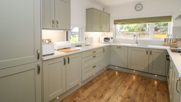 Una cocina moderna con armarios de tonos claros, encimera de madera, microondas, tostadora y ventana con vistas a zonas verdes.