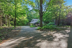 A house surrounded by a forested area with a gravel driveway leading to the entrance.