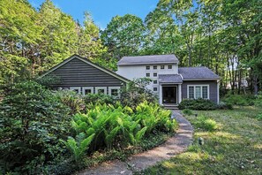A two-story house with a gravel driveway and lush greenery.