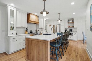 A modern kitchen with white cabinetry, a wooden island, bar stools, and stainless steel appliances.