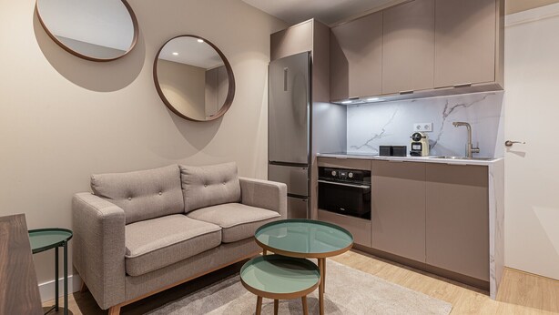 A compact living space with a sofa, a glass-top table, a kitchen with a refrigerator and stove, and two wall-mounted mirrors. - Waou Essence VI Antón Martín - Short Duration (Madrid)
