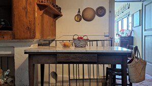 A kitchen with a wooden countertop, hanging pots, and a basket of oranges.