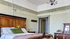 A bedroom with a bed, a sofa, a wooden dresser, and a chandelier.
