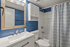 Une salle de bain avec un lavabo blanc, un miroir avec un cadre doré, une douche avec un rideau à rayures et des toilettes.