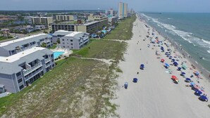 A coastal hotel with multiple buildings, a beach with umbrellas, and a view of the ocean. - Sea Cloisters II Ocean Front Beach Retreat (North Myrtle Beac)
