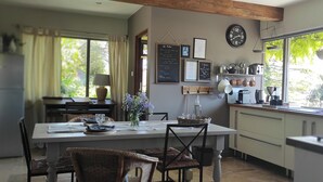 A modern kitchen with a dining area, featuring a large window, wooden beams, and a clock on the wall. - Charming gîte nestled in the heart of the Opal valleys, near Montreuil/mer (Marenla)