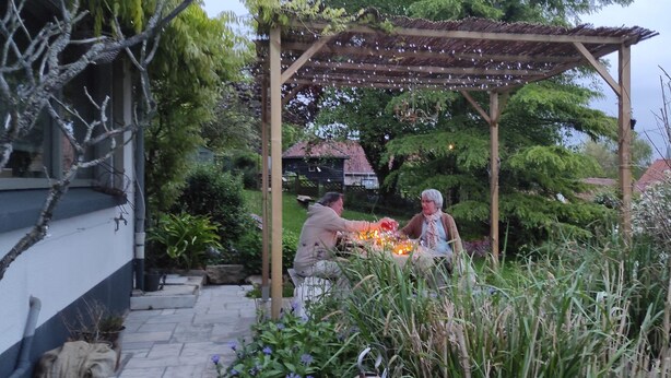 A wooden pergola with string lights, surrounded by lush greenery and a stone pathway. - Charming gîte nestled in the heart of the Opal valleys, near Montreuil/mer (Marenla)