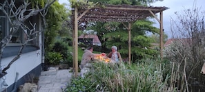 Uma pérgola de madeira com luzes de corda, rodeada por vegetação exuberante e um caminho de pedra.