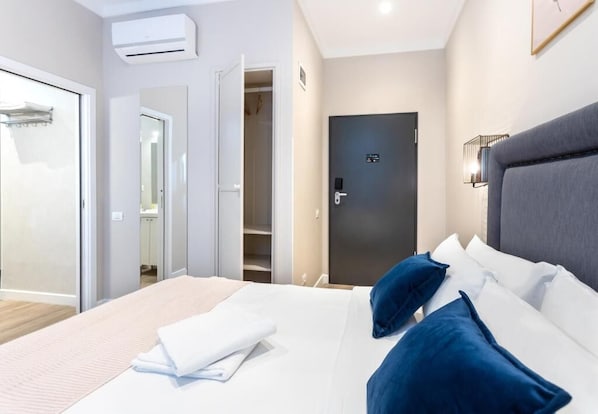 A hotel room with a bed, a wardrobe, a door, and an air conditioning unit.