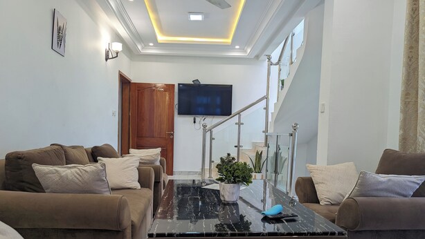A modern living room with a sofa set, a coffee table, and a TV mounted on the wall. - Luxery 3-bedroom villa with ACs in a secure and assessable neighborhood in Limbe (Limbe)