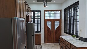 A modern kitchen with wooden cabinets, a stainless steel refrigerator, a marble countertop, and a large window with a metal grille. - Luxery 3-bedroom villa with ACs in a secure and assessable neighborhood in Limbe (Limbe)