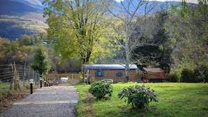 Un chalet rustique, accessible par un chemin de gravier, entouré d  ’arbres et adossé à un paysage montagneux.