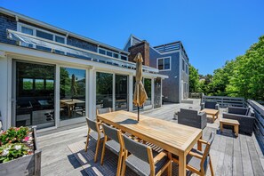 Une maison moderne dotée d’une terrasse en bois, de mobilier d’extérieur et d’une porte vitrée donnant sur un patio.