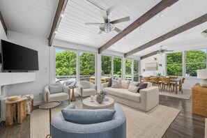 A spacious living area with a large TV, comfortable seating, and a dining area with natural light and outdoor views. - Luxury Coastal Retreat in the Private Gated Community (2426) (West Yarmouth)