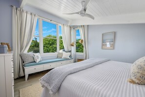 A bedroom with a bed, a window seat, a ceiling fan, and a view of greenery. - Luxury Coastal Retreat in the Private Gated Community (2426) (West Yarmouth)