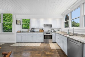 A kitchen with white cabinets, granite countertops, stainless steel appliances, and large windows. - Luxury Coastal Retreat in the Private Gated Community (2426) (West Yarmouth)
