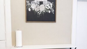 Une pièce avec un bureau blanc, deux chaises blanches, une œuvre d’art florale en noir et blanc encadrée au-dessus du bureau, et une porte blanche sur la droite.