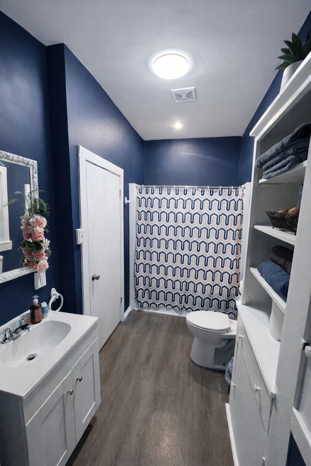 A bathroom with a blue wall, white fixtures, a patterned shower curtain, and a white toilet.