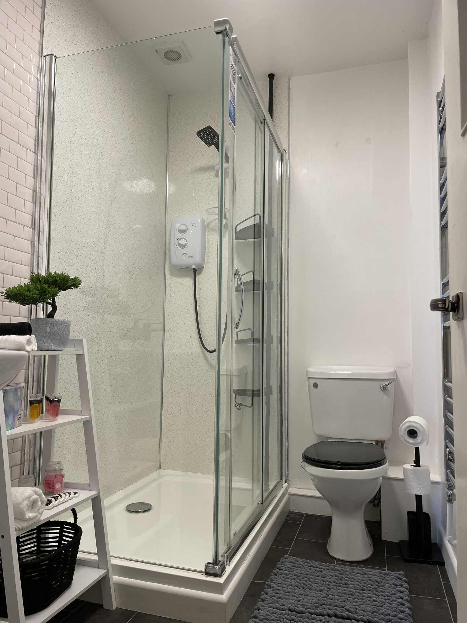 Et moderne badeværelse med et glasvægshus, et hvidt toilet og en lille hylde med toiletartikler.