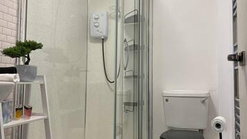 Et moderne badeværelse med et glasvægshus, et hvidt toilet og en lille hylde med toiletartikler.