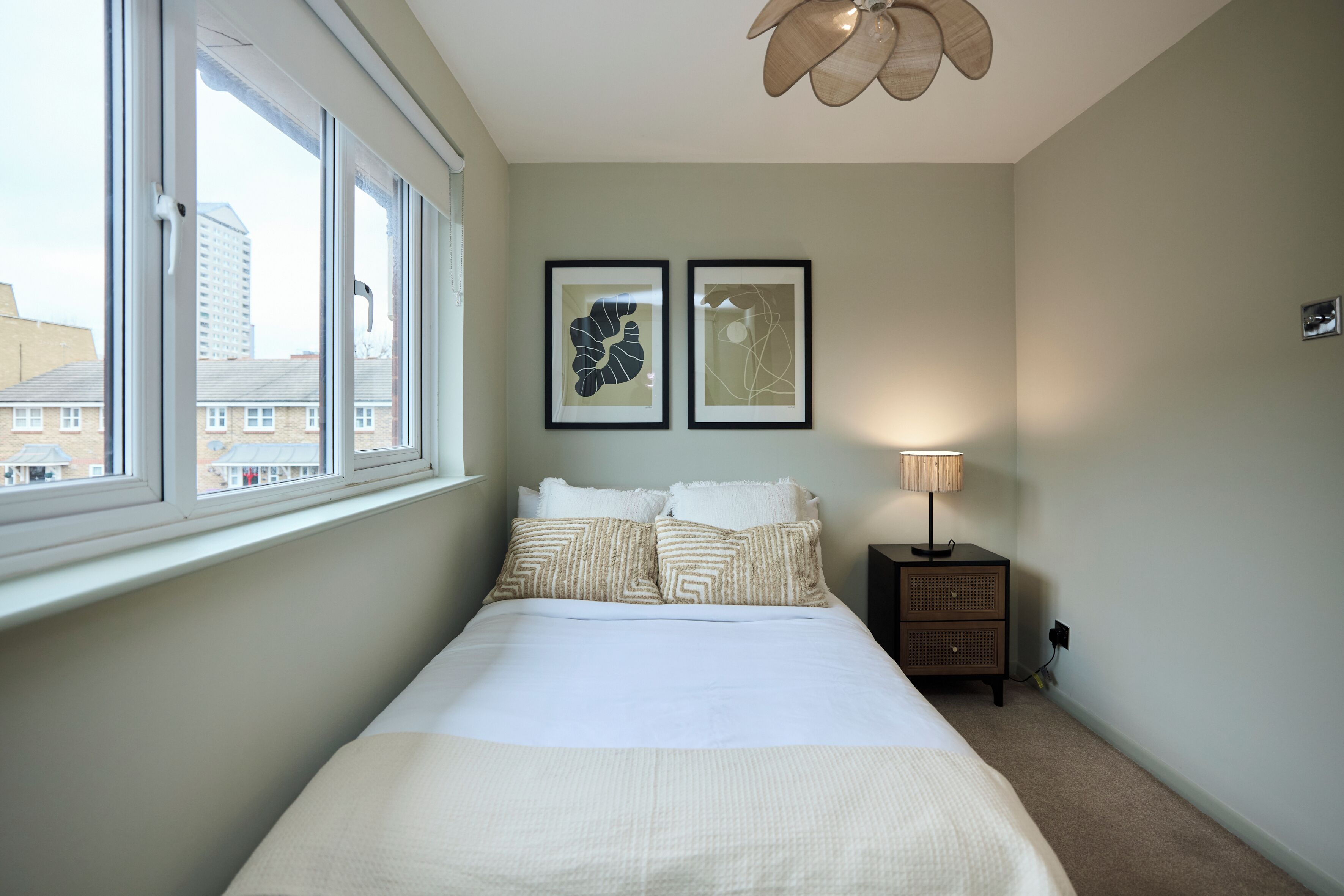 Un dormitorio con una cama grande, una ventana, una mesita de noche y dos cuadros enmarcados en la pared.