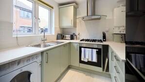 A compact kitchen with a washing machine, a gas stove, and a built-in oven. - Poplar Garden Townhouse (London)
