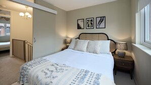 A bedroom with a large bed, bedside tables with lamps, a headboard, and wall art. - Poplar Garden Townhouse (London)