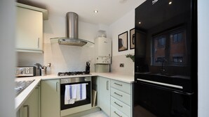 A modern kitchen with a built-in oven, a stainless steel range hood, and a black refrigerator. - Poplar Garden Townhouse (London)