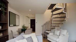 A modern living room with a staircase, a sofa, a coffee table, and a bookshelf. - Poplar Garden Townhouse (London)